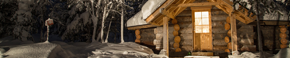 A snow-covered log wilderness cabin lit up at night in Enontekiö