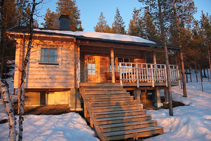 A wooden wilderness cabin in the snow, golden evening light on the timber and deck